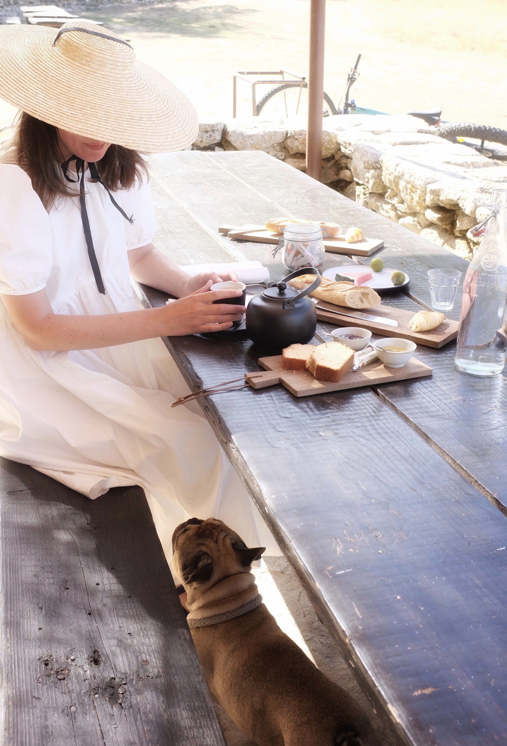 A woman in a straw hat at a table, a dog waiting beside her
