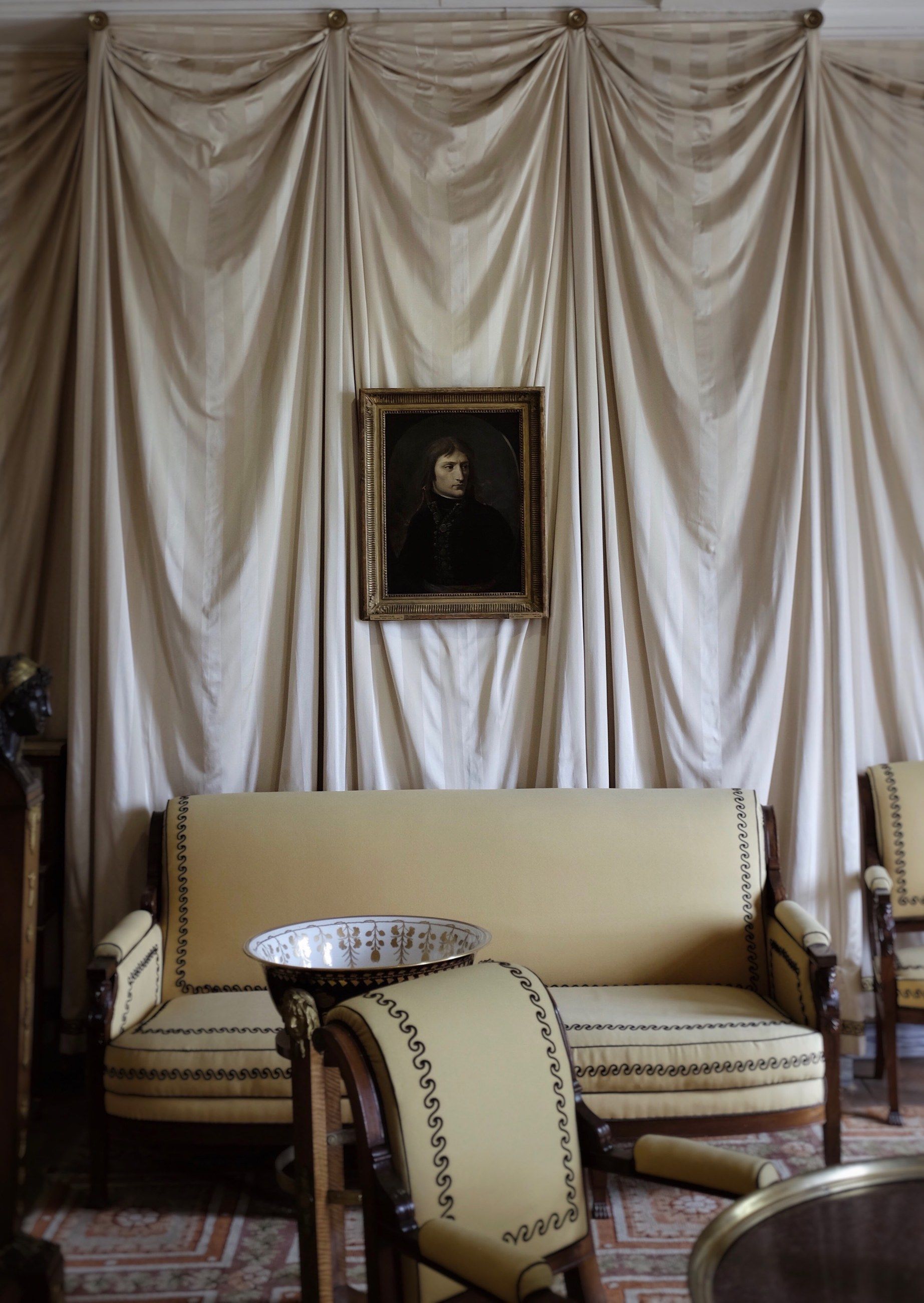 A château salon with draped fabric walls, a portrait painting and a striped sofa