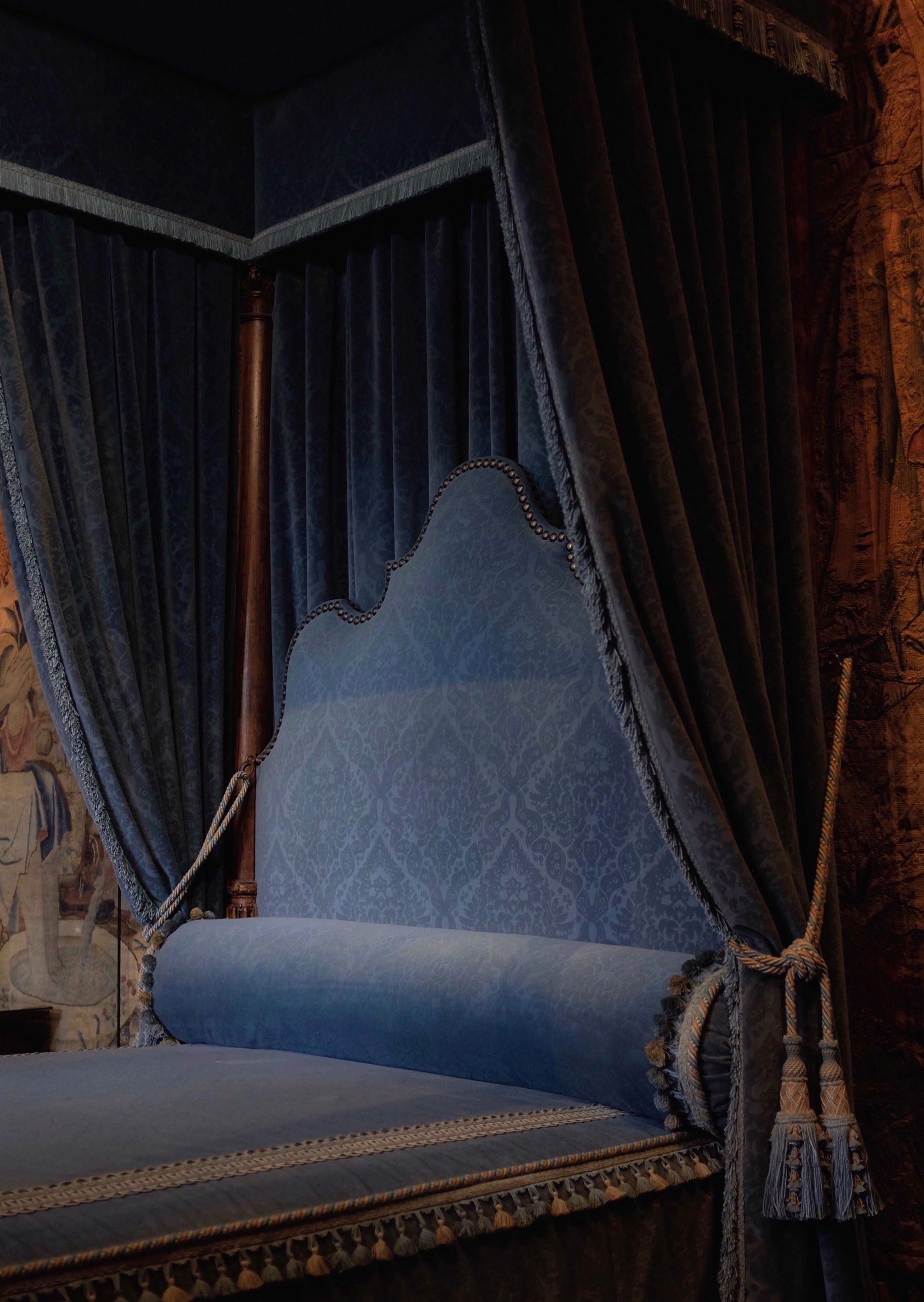 A bed hung with blue damask curtains